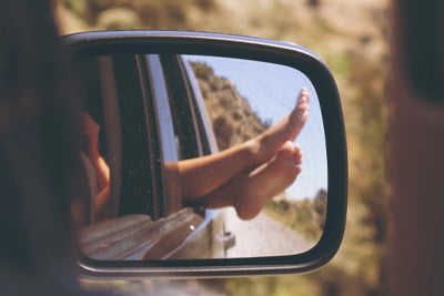 Car side mirror with the reflection of someone's legs sticking out the window